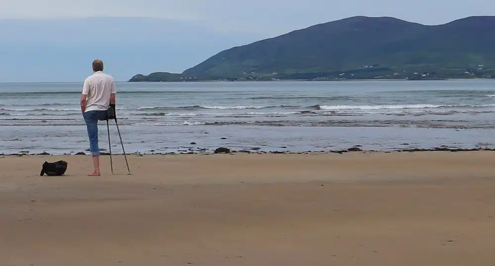 Man with one leg and crutches stands on a beach