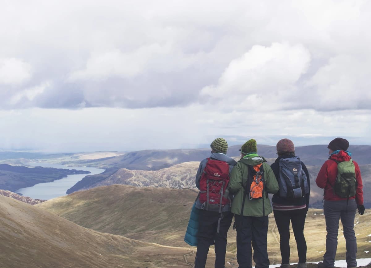 Four people in winter coats look out over a mountain valley