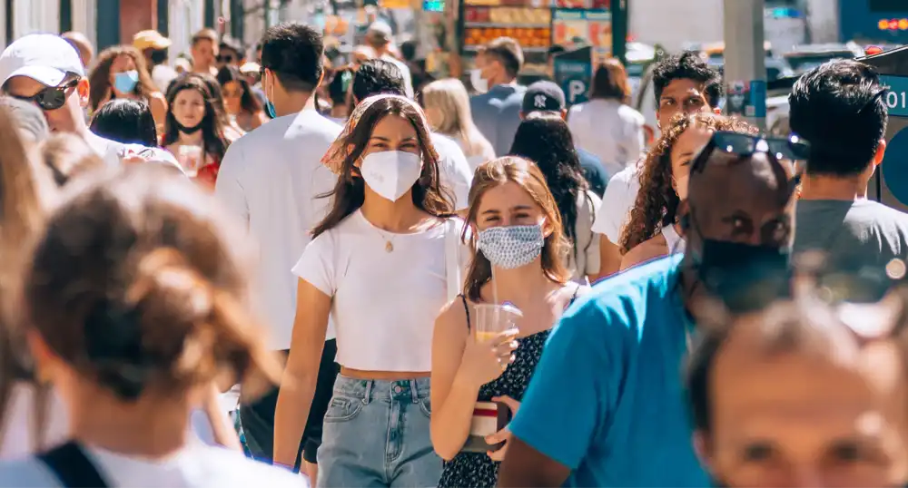 People walk on crowded street, wearing face masks