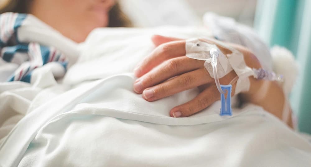 Closeup of a person's hand with an IV in it as they lay in a hospital bed