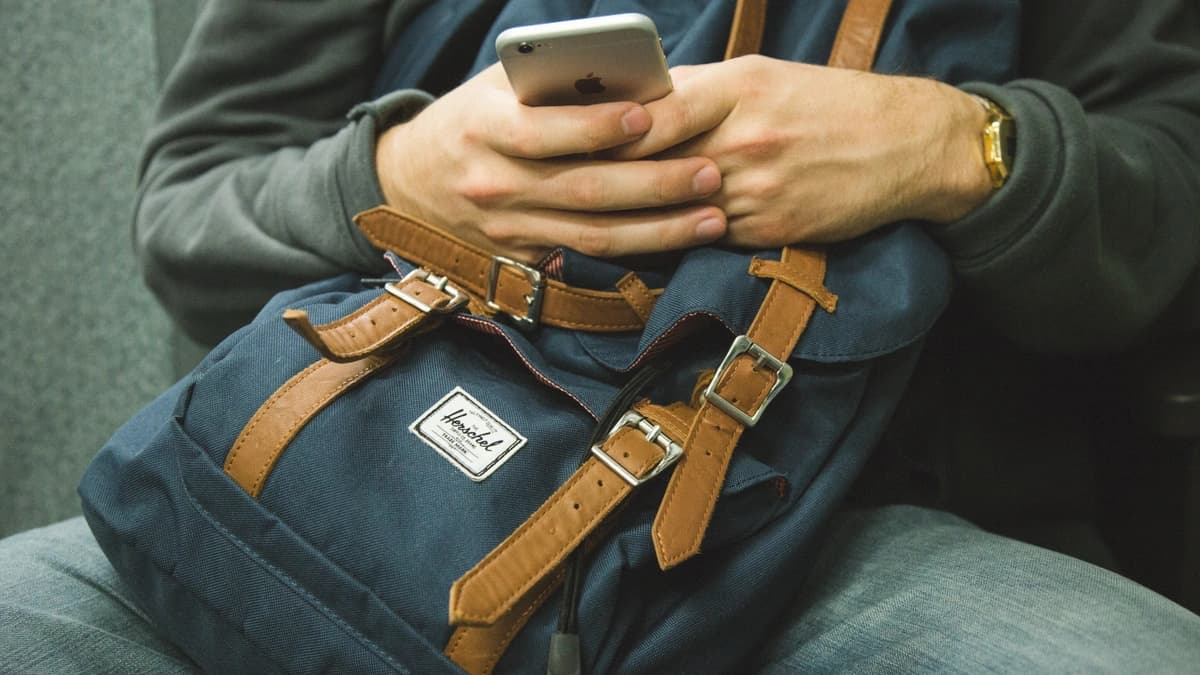 Person uses their cell phone with a backpack on their lap