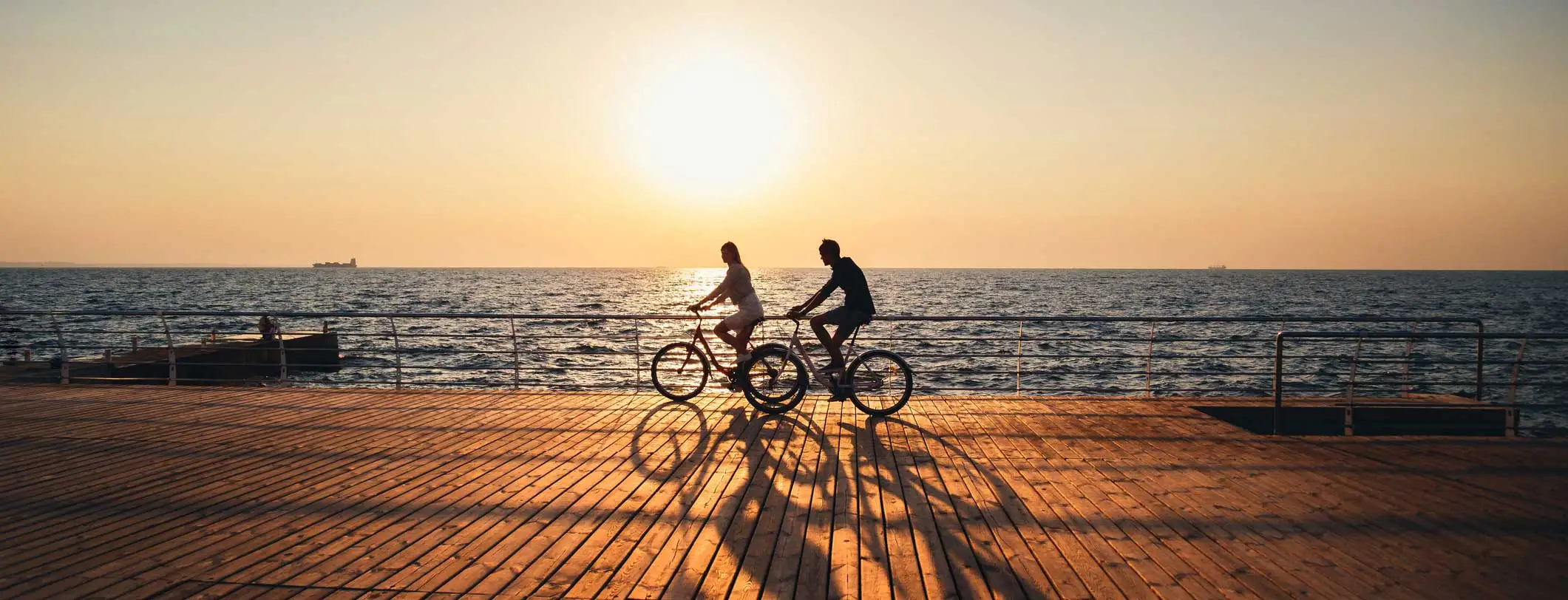 Two people ride bikes on a beach boardwalk