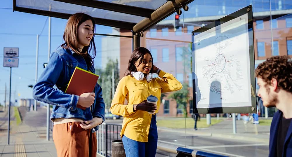 Three students sit at a bus stop