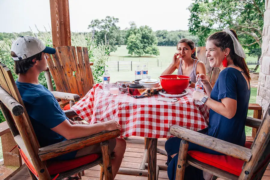 Three teenagers sit at a patio table, laughing together