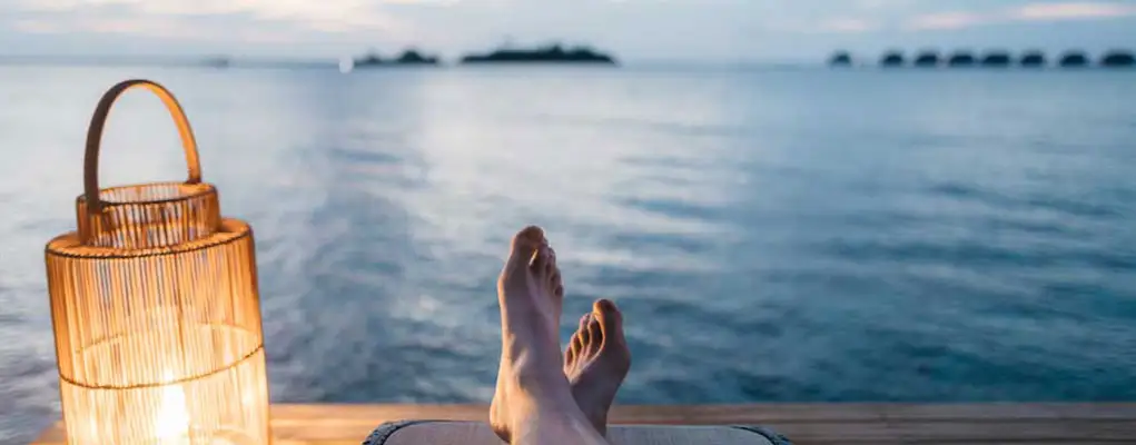 Person sits on a lakeside dock with feet up, relaxing